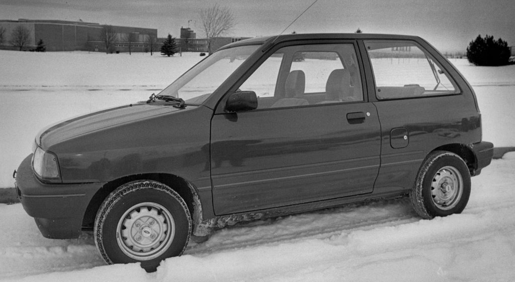 A black and white photo of a Ford Festiva compact car in the snow