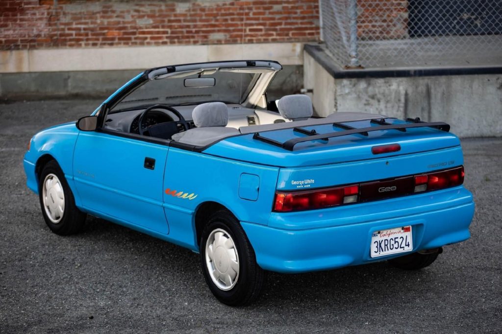 The rear 3/4 view of a blue 1992 Geo Metro LSi Convertible parked by a brick building