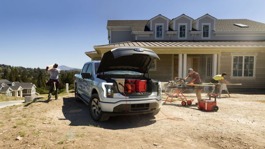 Workers at a home construction site run power tools and store items in a silver 2022 Ford F-150 Lightning XLT