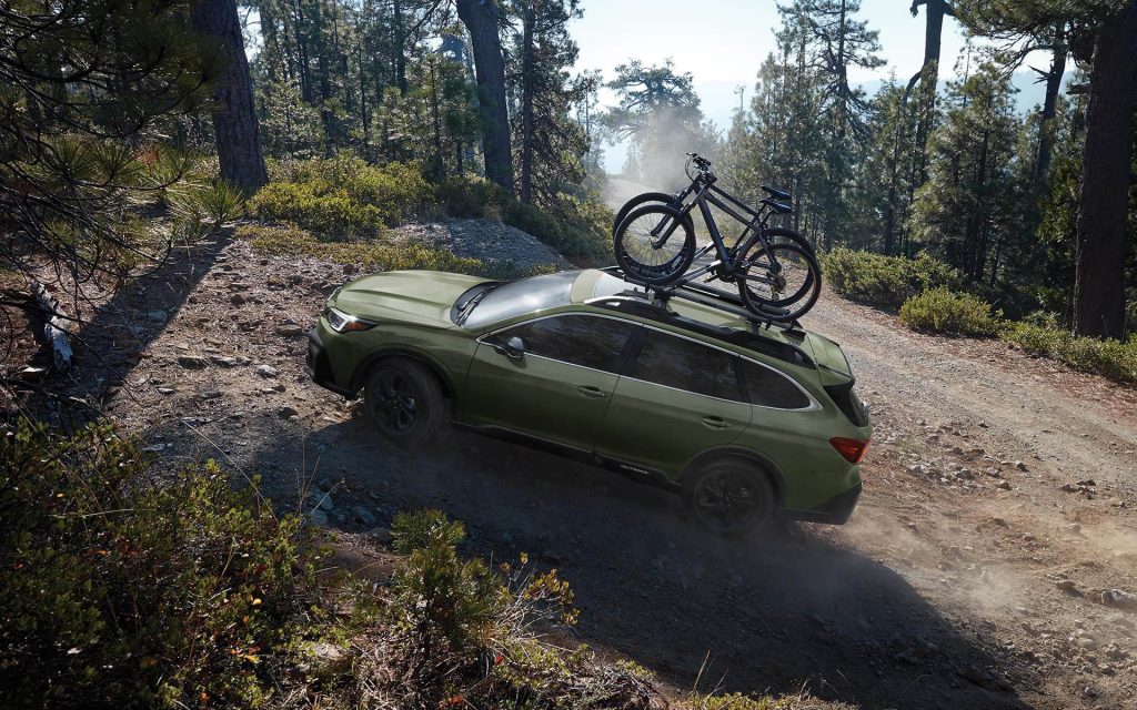 a green subaru outback with bikes on top climbing a forested hill