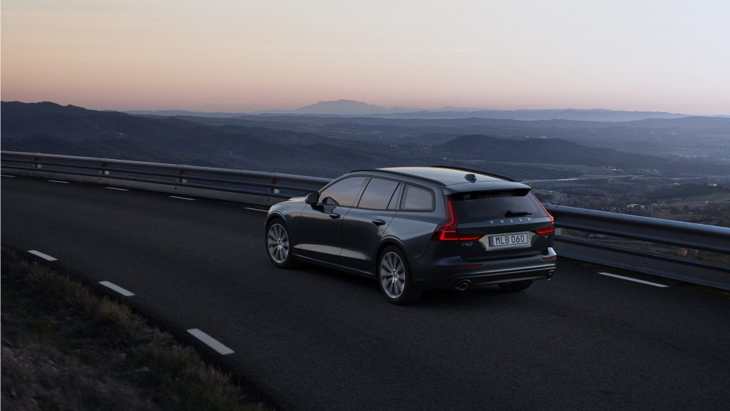 A dark blue Volvo V60 on a mountain road at sunset, photographed from the rear