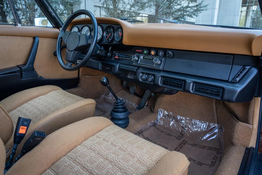 The tan-cloth front seats and black-and-tan dashboard of a 1975 Porsche 911 S