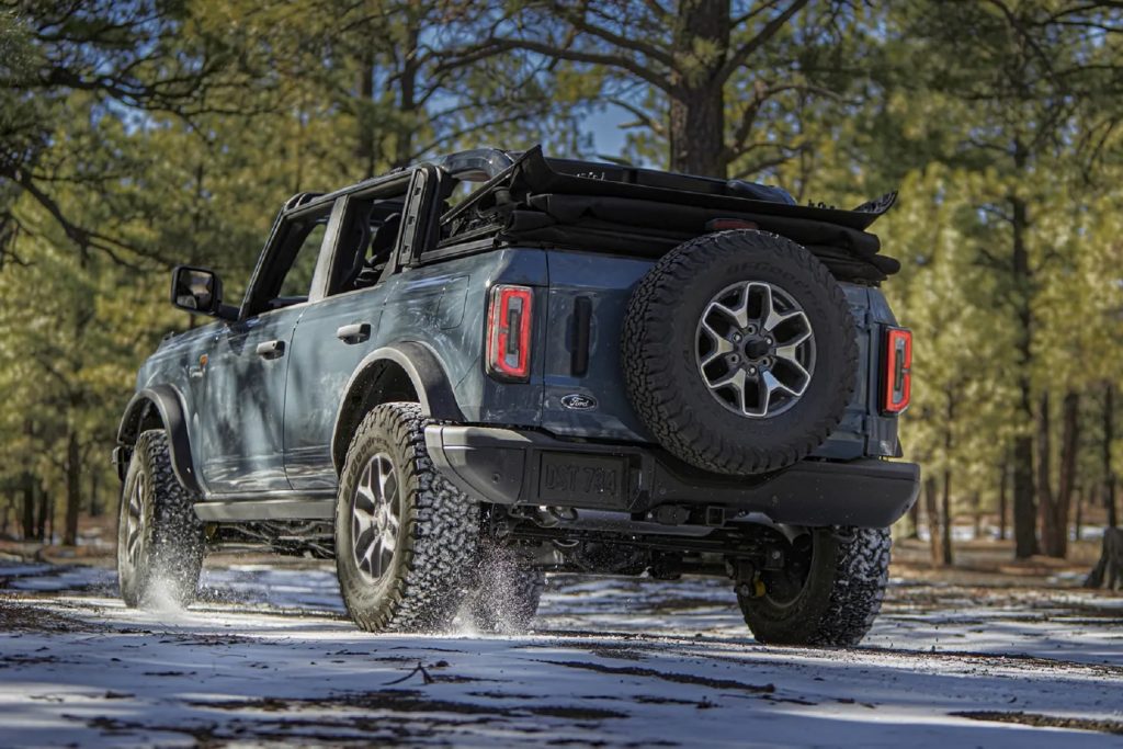 The rear 3/4 view of a bluish-gray 2021 Ford Bronco 4-Door Badlands with its roof down in a snowy forest