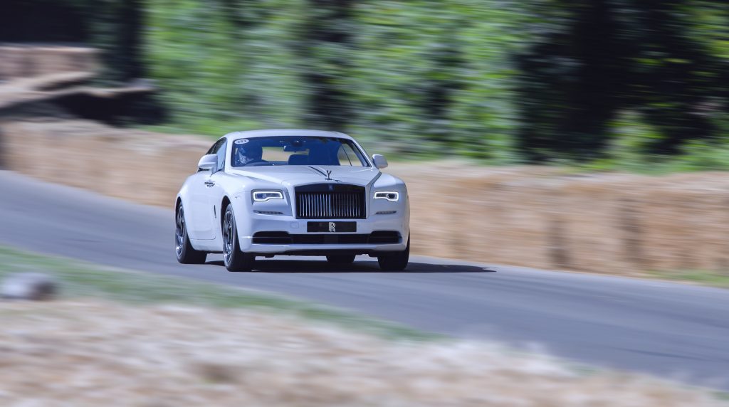 A white Rolls-Royce Wraith coupe driving down a tree-lined road