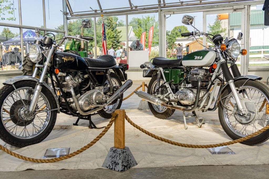 A black-and-gold 1974 Norton Commando 850 to the left of a green-and-white 1971 BSA A65 Thunderbolt at IMS Outdoors Chicago 2021